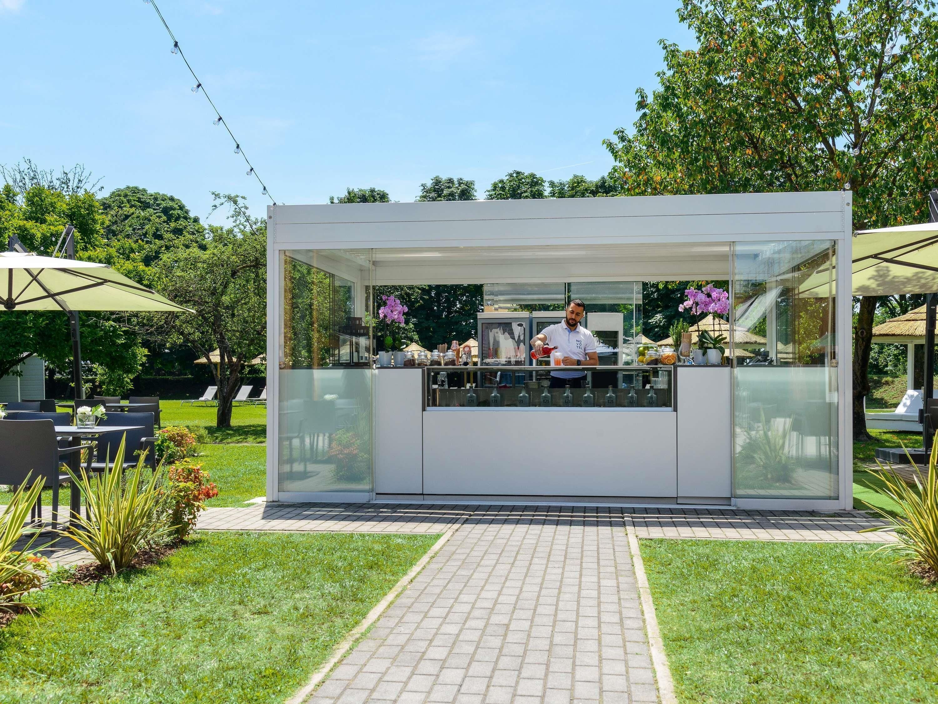 A modern outdoor bar with a glass enclosure, a bartender, and outdoor seating.