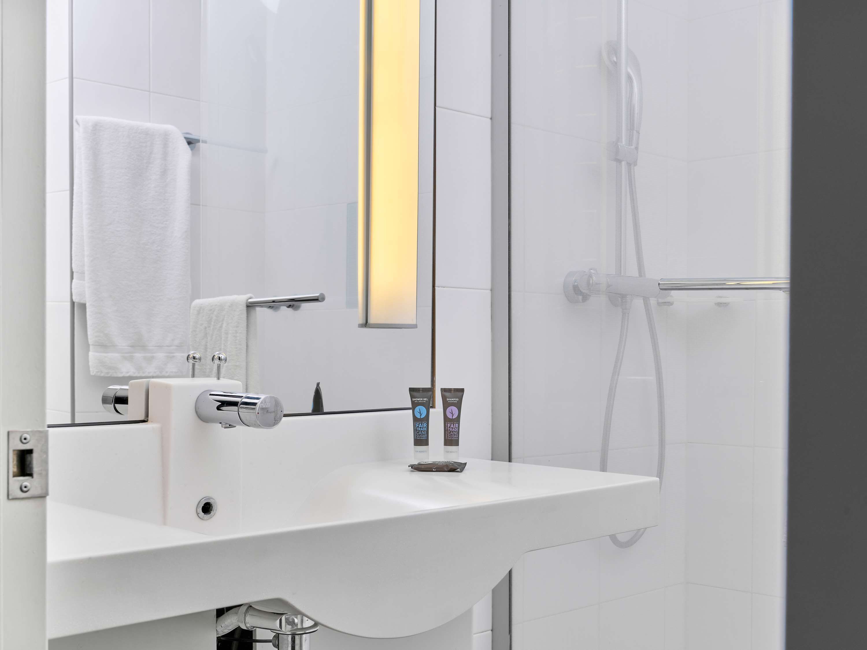 Un baño moderno con lavamanos blanco, un espejo y zona de ducha.