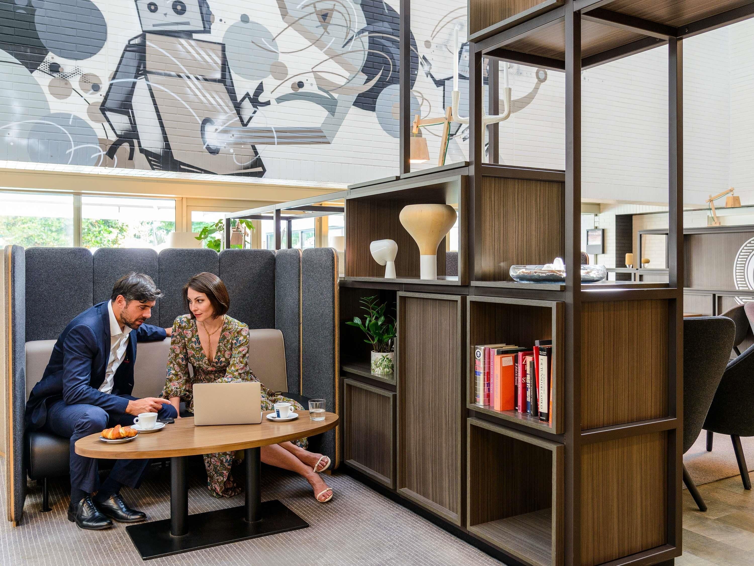 Un espace de bureau moderne doté d’un espace de réunion comprenant une table ronde, deux chaises, une bibliothèque et une fresque murale décorative.