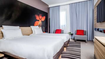 Ein Hotelzimmer mit einem großen Bett, einem Schreibtisch, zwei Stühlen, einem Fernseher und einem Bild an der Wand.