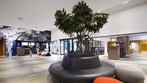 A modern lobby with a curved black sofa, a large potted tree, and a wooden reception desk.