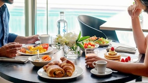 A dining table with breakfast items, a bottle, and a flower arrangement.