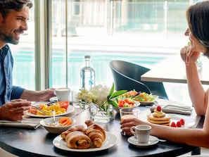 Una mesa de comedor con alimentos para el desayuno, una botella y un arreglo floral.