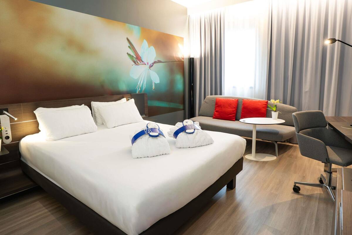 A hotel room with a large bed, a sofa, a small table, and a chair.