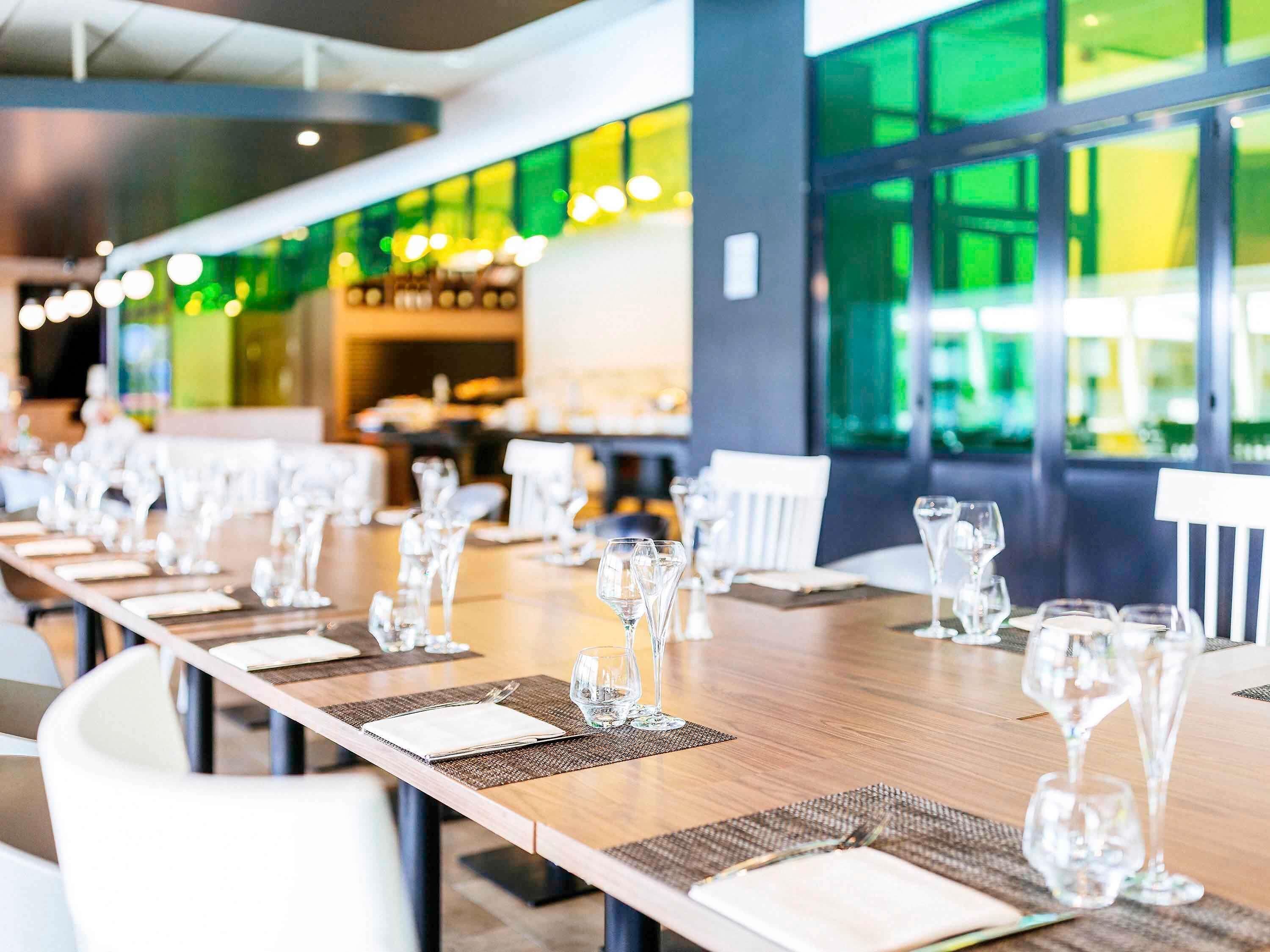 Un restaurante con mesas largas dispuestas para comer, copas de vidrio transparentes y vistas amplias a través de grandes ventanales.