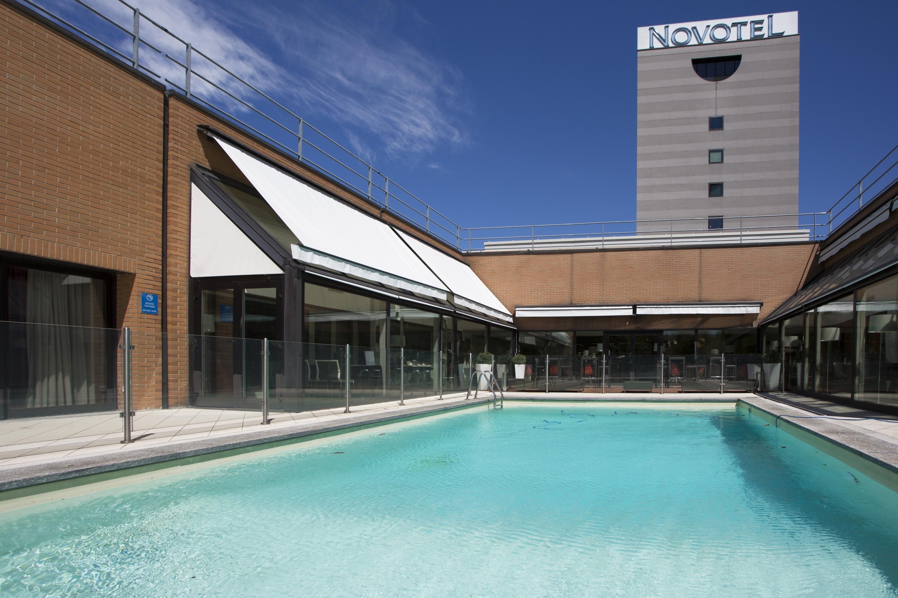 A swimming pool area with a Novotel hotel in the background.