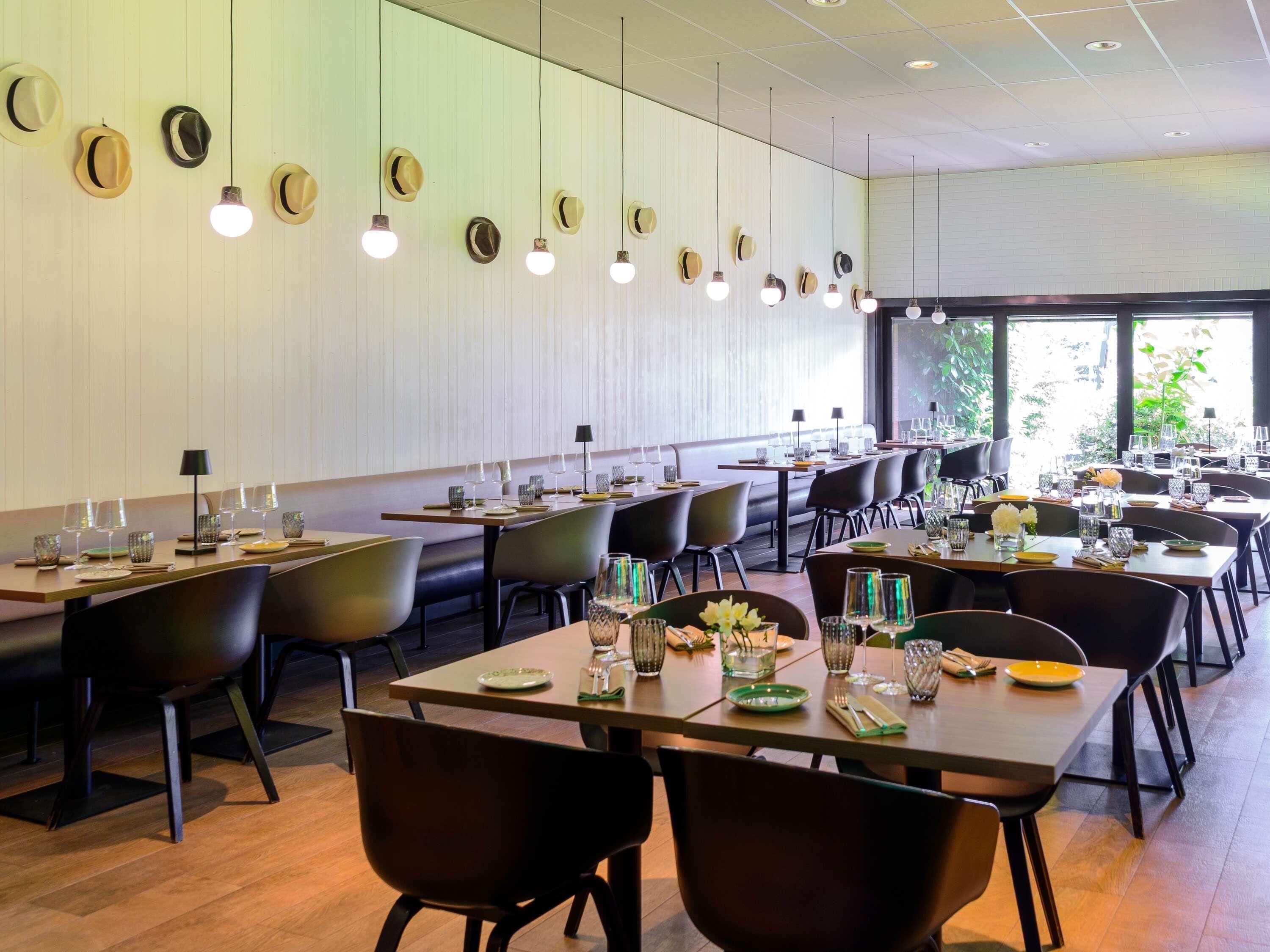 Un restaurante moderno con mesas largas, sillas negras y una fila de sombreros colgados en la pared.