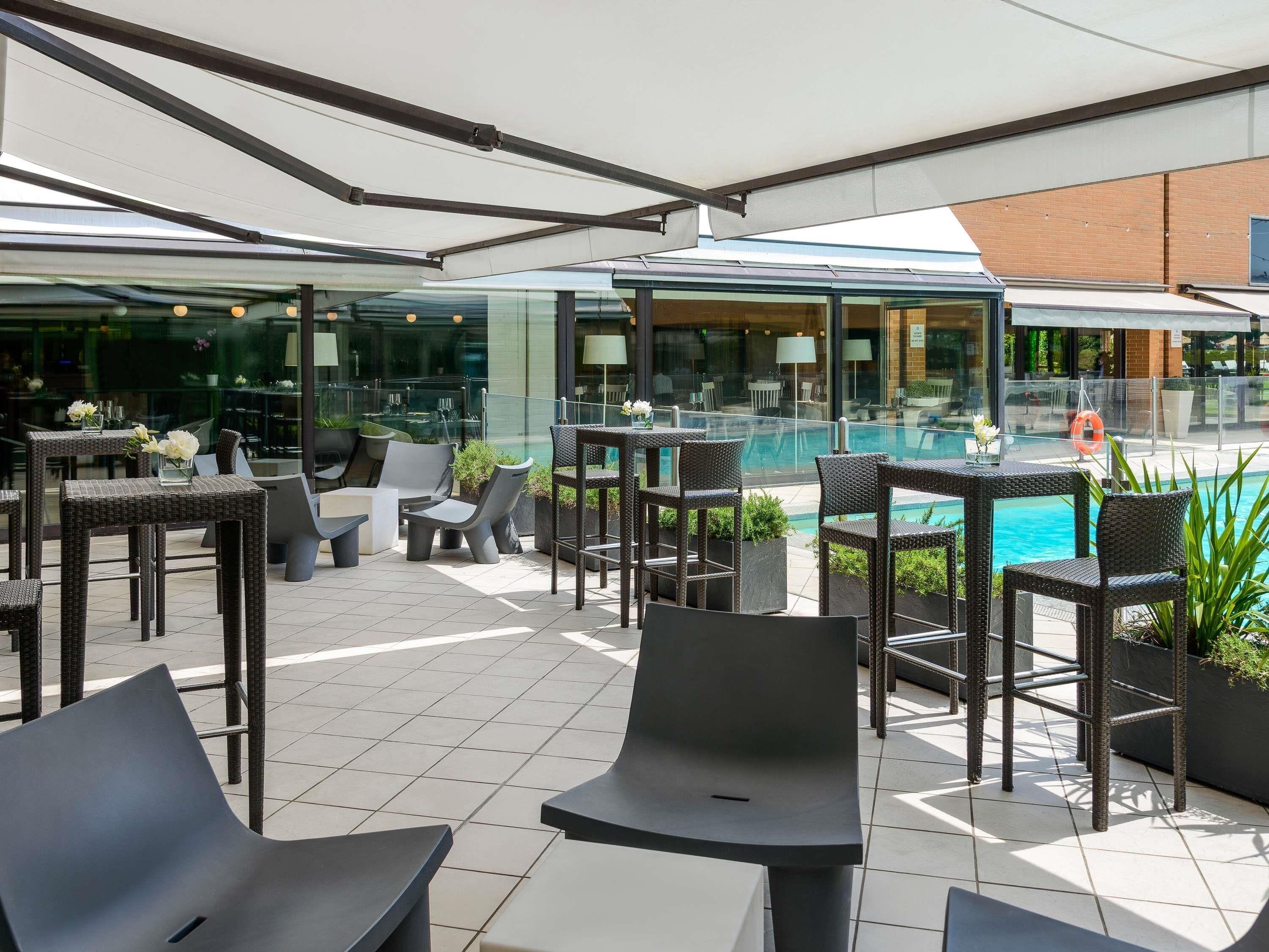 Een terras buiten met rieten meubilair, een zwembad en een glazen omheining.