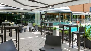 Een terras buiten met rieten meubilair, een zwembad en een glazen omheining.