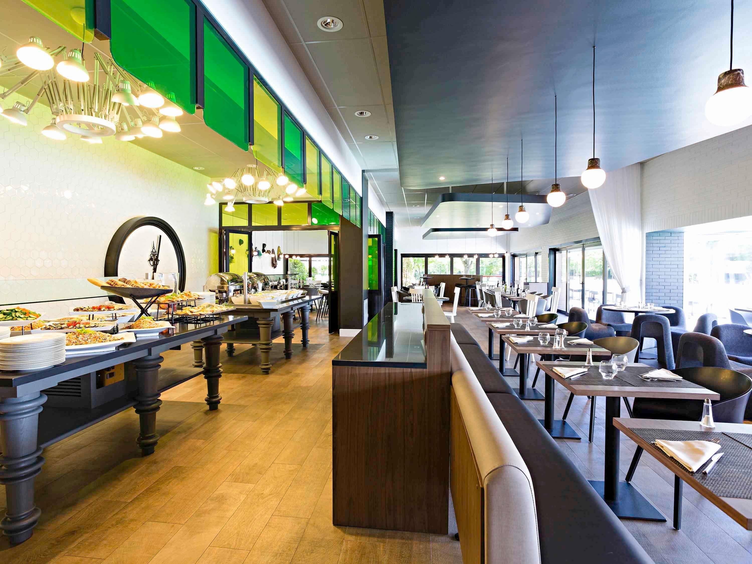Un comedor moderno con barra libre, diferentes disposiciones de mesas y vistas al exterior.