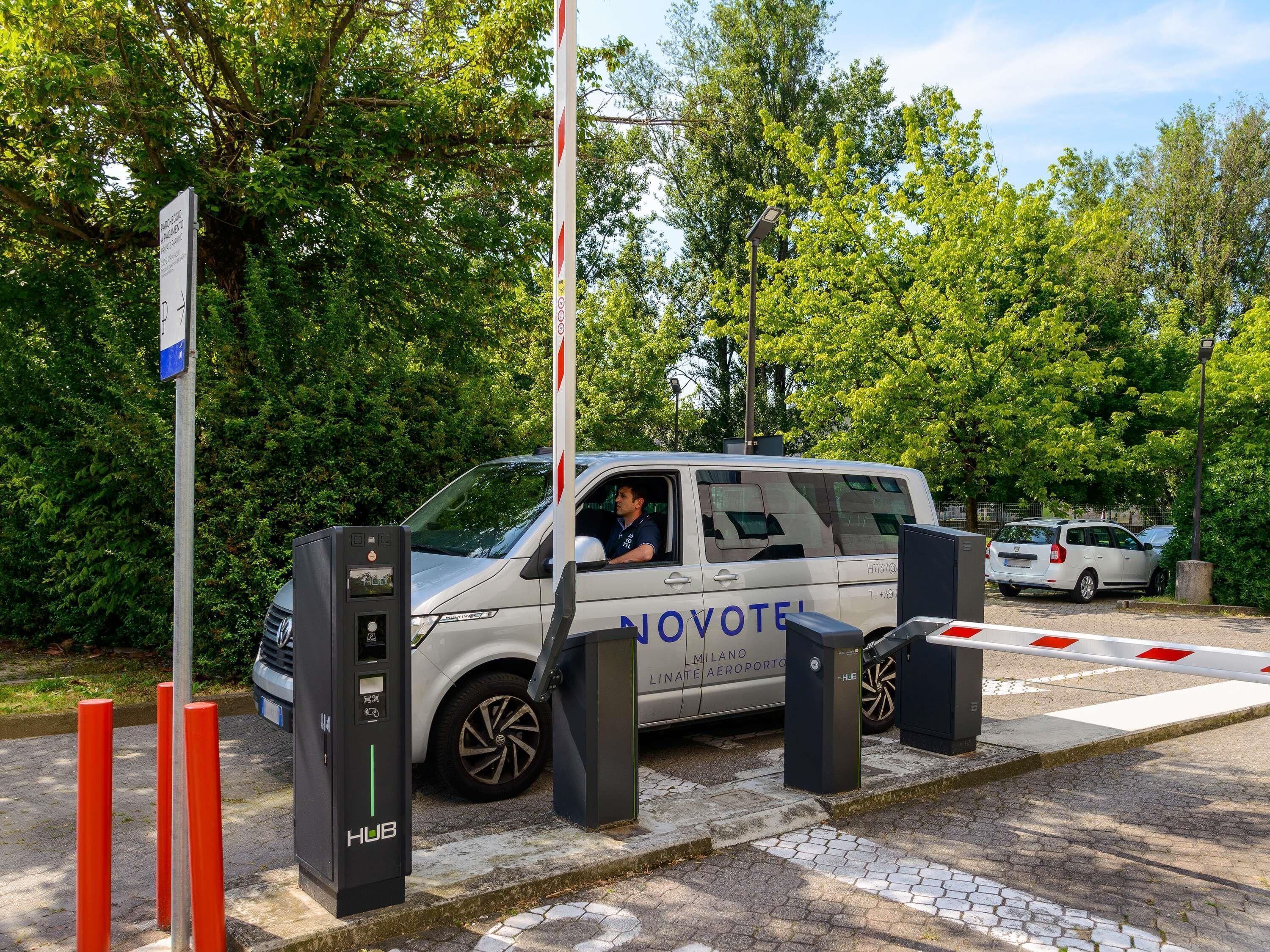 Un veicolo parcheggiato presso una stazione di ricarica, con un segnale 'NOVOTEL', che indica un albergo o una sistemazione nelle vicinanze.