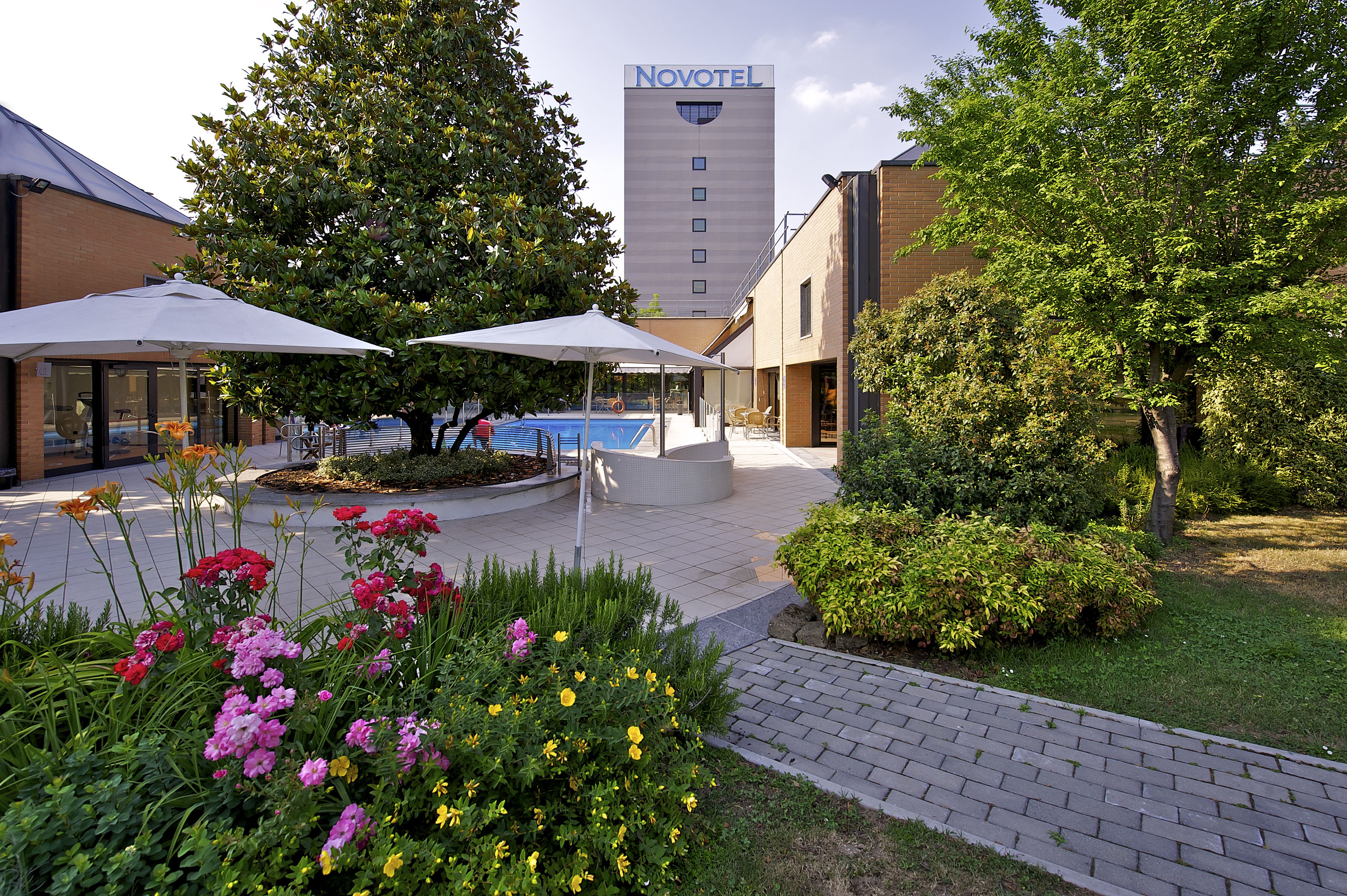 Pátio de hotel com área de estar externa, piscina e edifício da Novotel ao fundo.