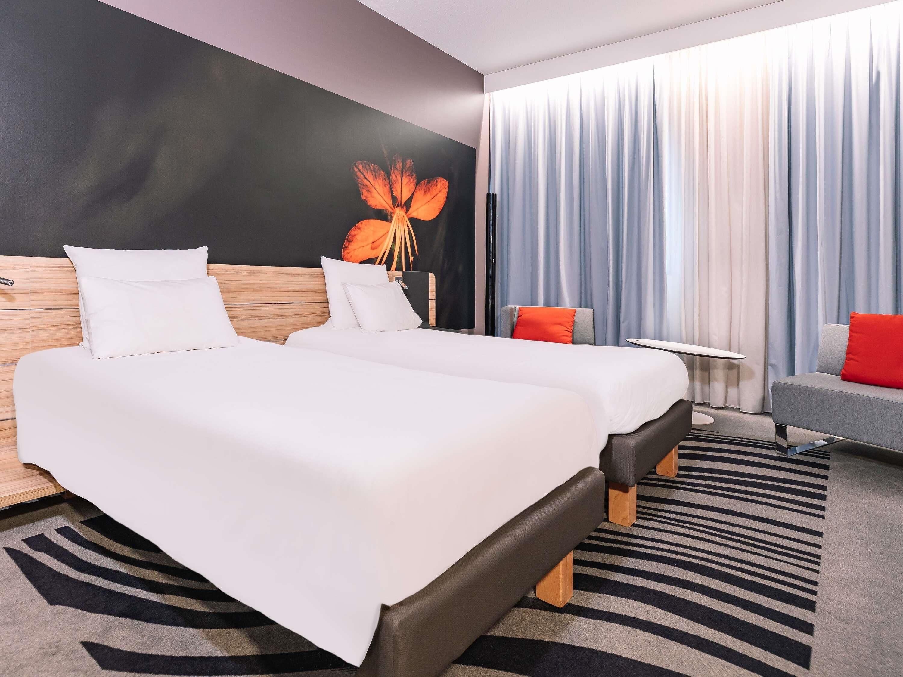 Una camera d'albergo con due letti, un divano, un tavolino e un quadro floreale appeso al muro.
