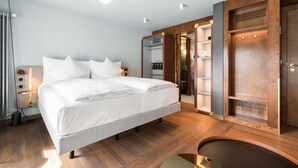 Ein modernes Hotelzimmer mit einem großen Bett, Holzboden, einem begehbaren Kleiderschrank und einem Schreibtisch mit Lampe.
