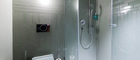 A modern bathroom with a glass-enclosed shower, a toilet, and a soap dispenser.
