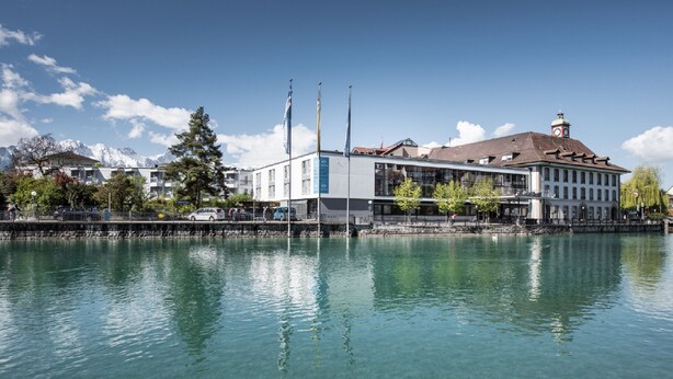 Ein Hotel am Wasser mit freiem Blick auf das Wasser, einem Glockenturm und Bergen im Hintergrund.