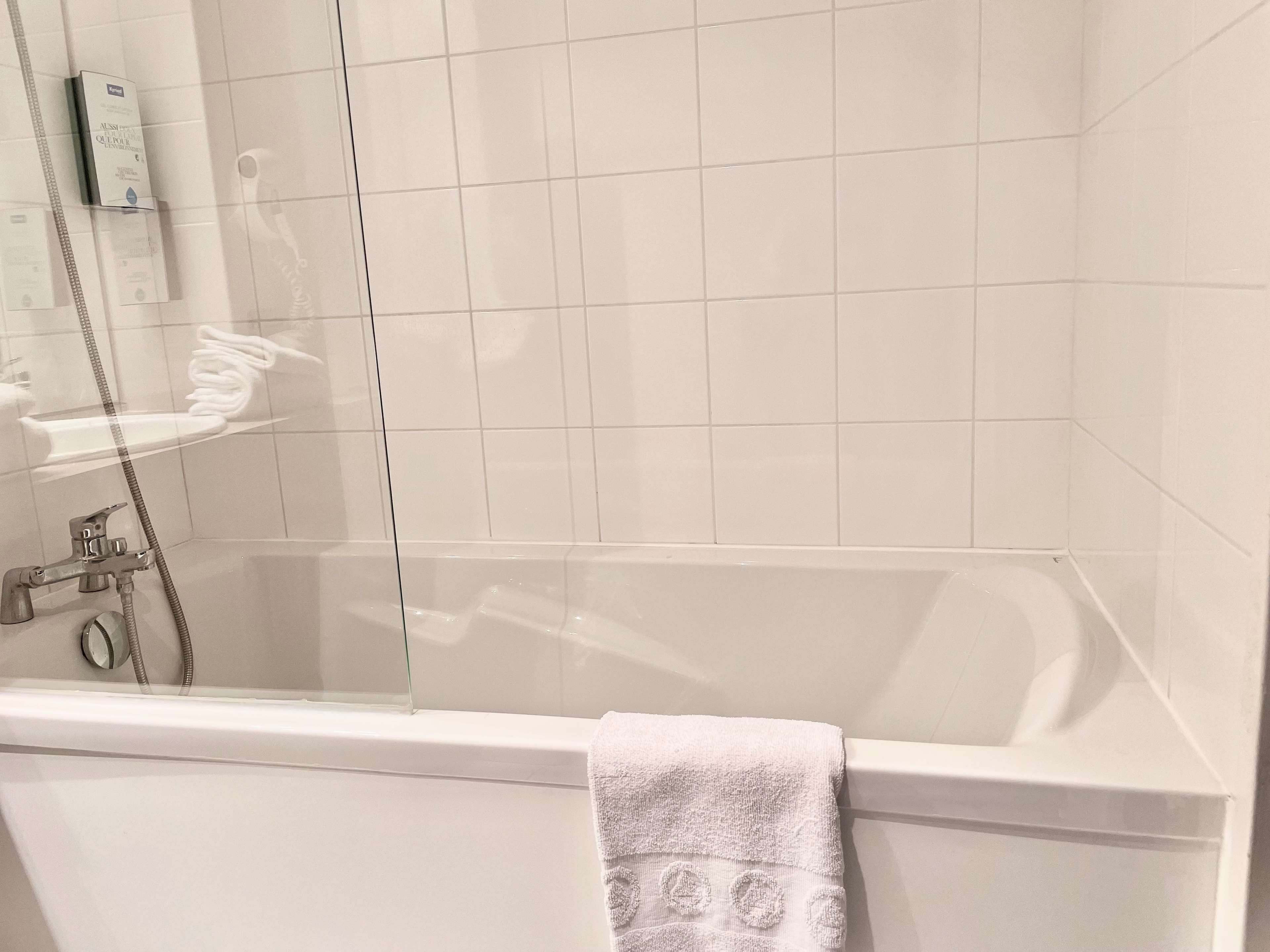 Un baño con bañera, ducha con mampara de vidrio y una toalla colgada a un lado.