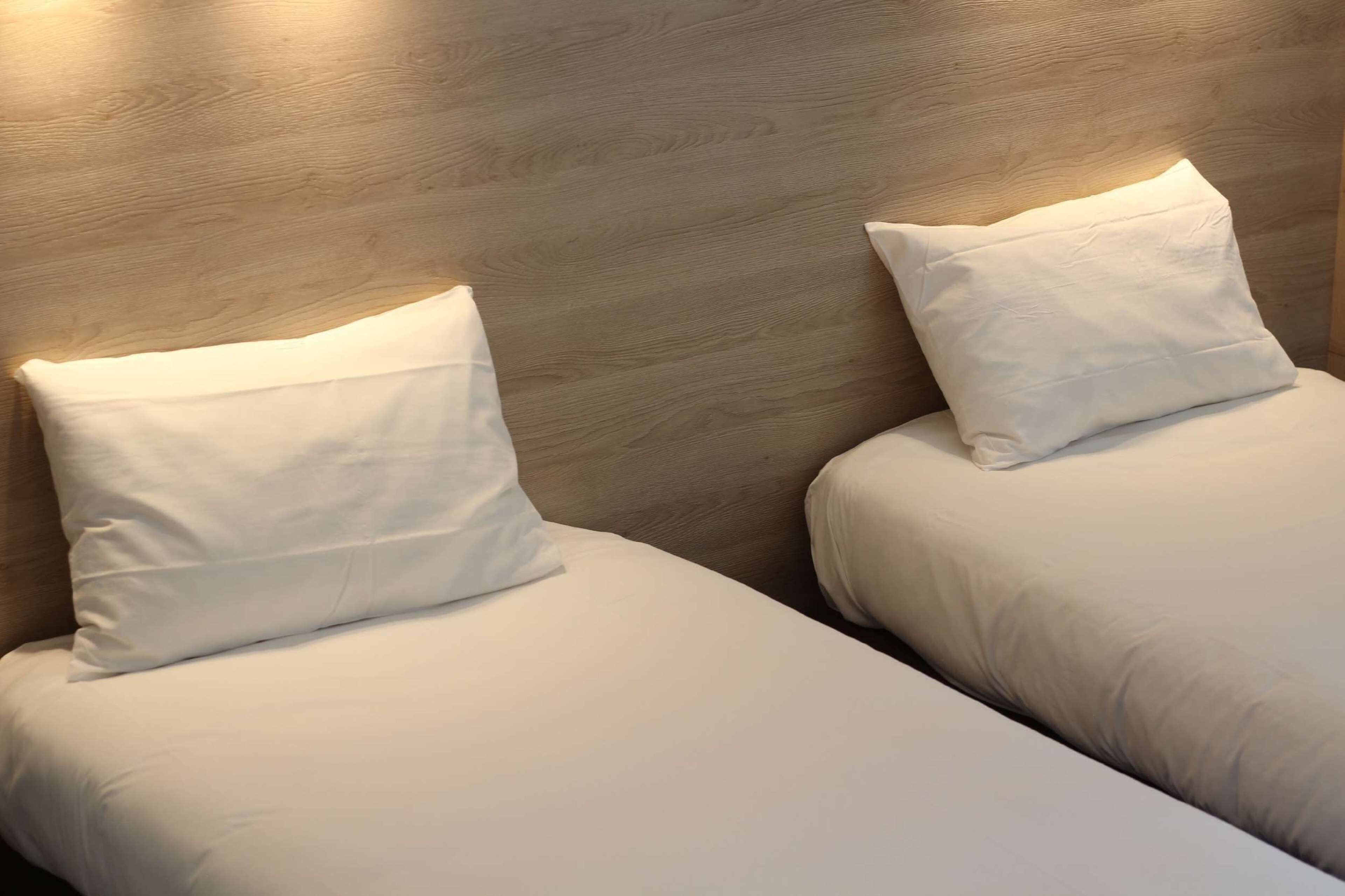 Dos camas individuales con sábanas y almohadas blancas, frente a un cabecero de madera.