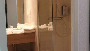 Une salle de bain avec une douche à parois de verre, un lavabo avec un miroir et des serviettes soigneusement pliées.