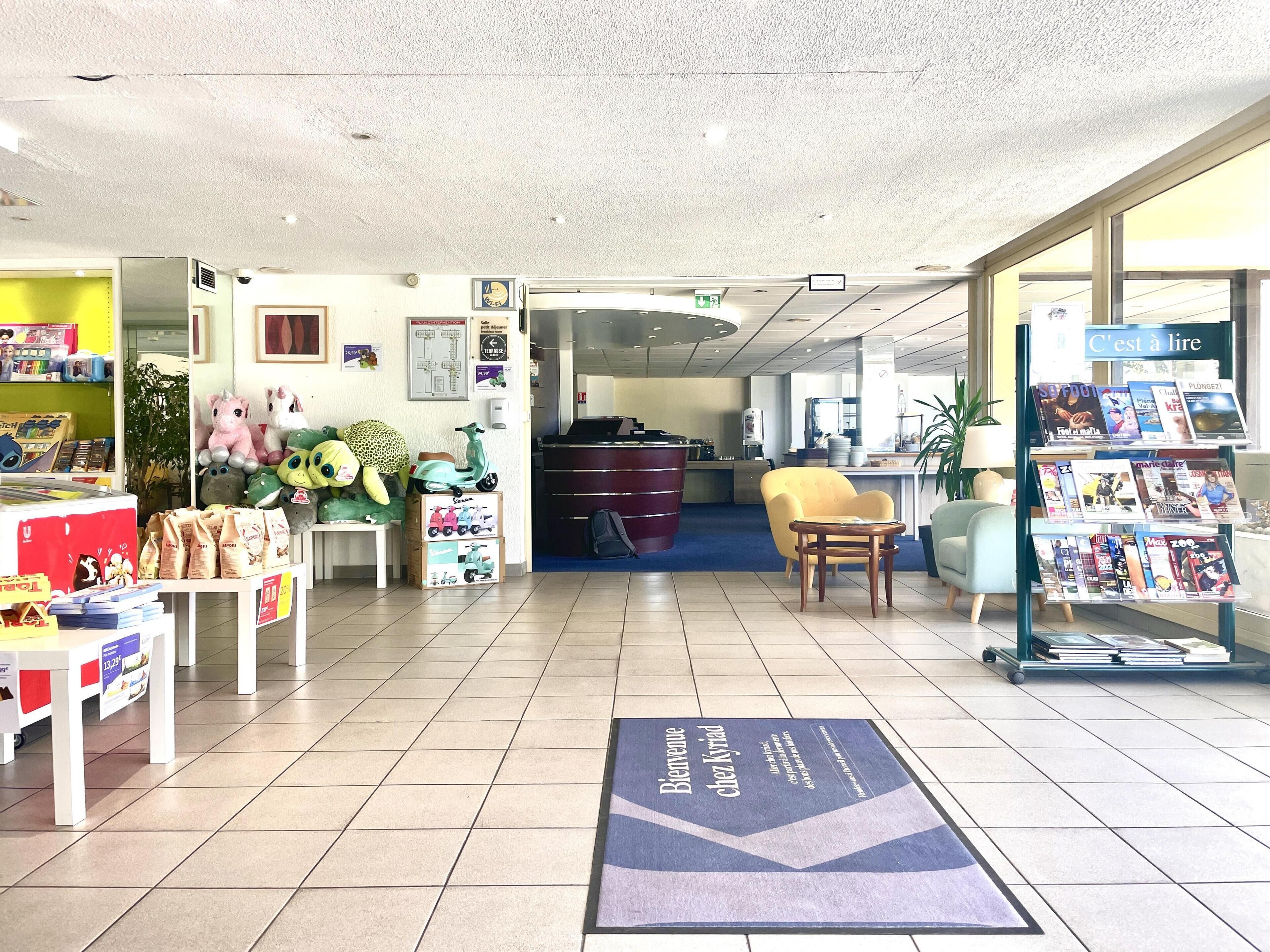 Un espace d’accueil avec un paillasson, des peluches, un coin salon et un présentoir à magazines.