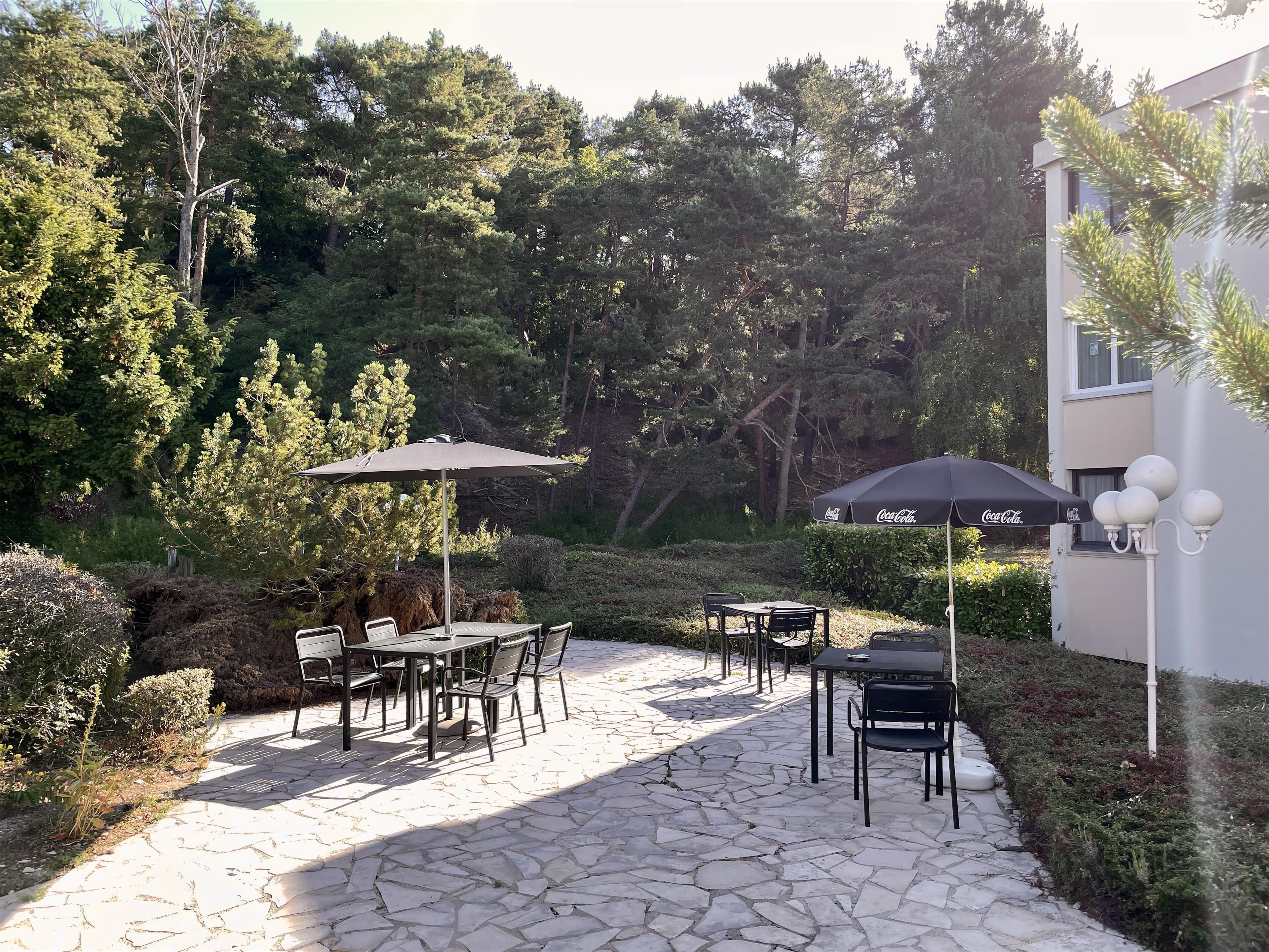 Une terrasse extérieure avec un sol en pierre, des tables, des chaises et des parasols.