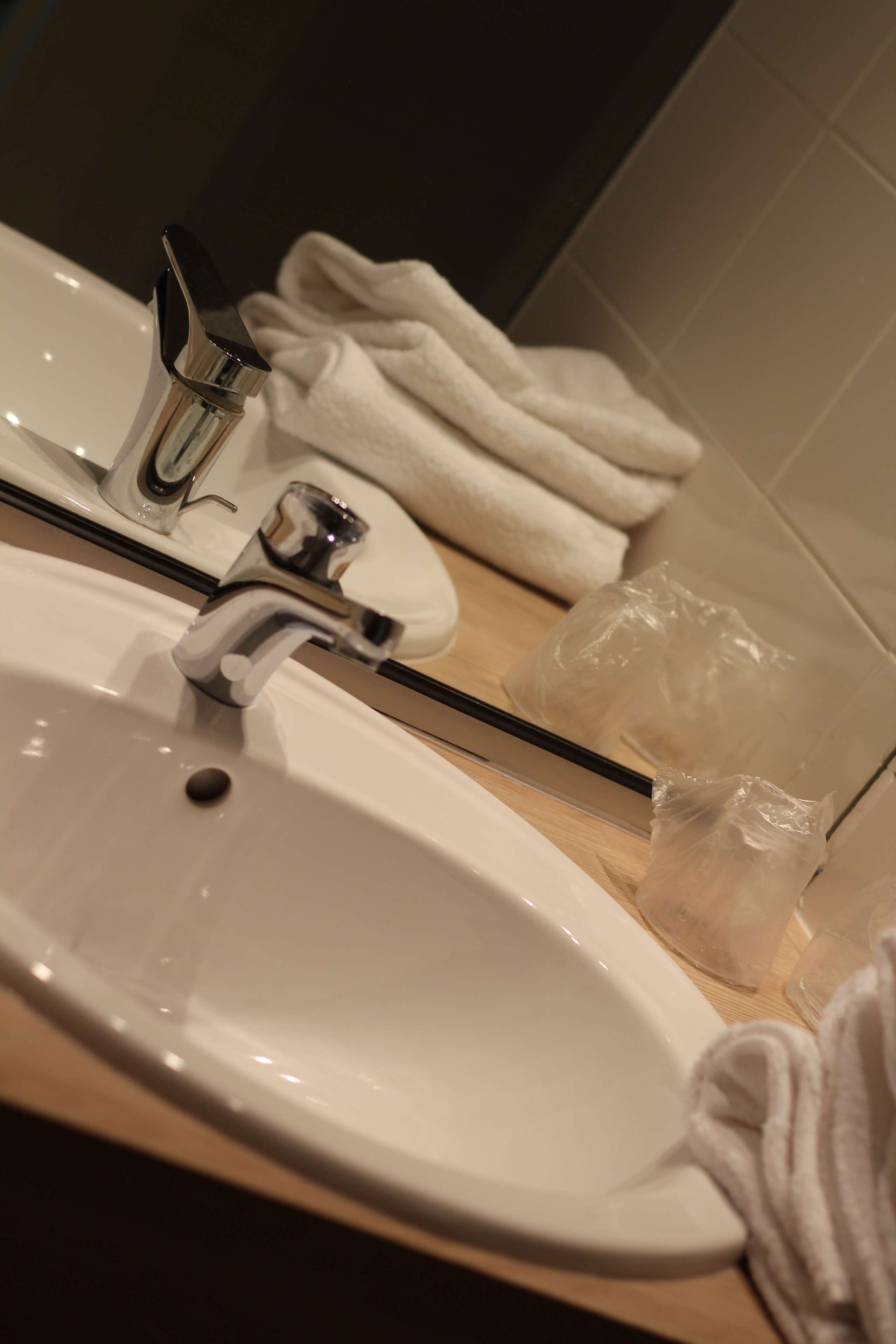 Un lavabo con grifo de cromo, un espejo y un toallero con toallas dobladas.
