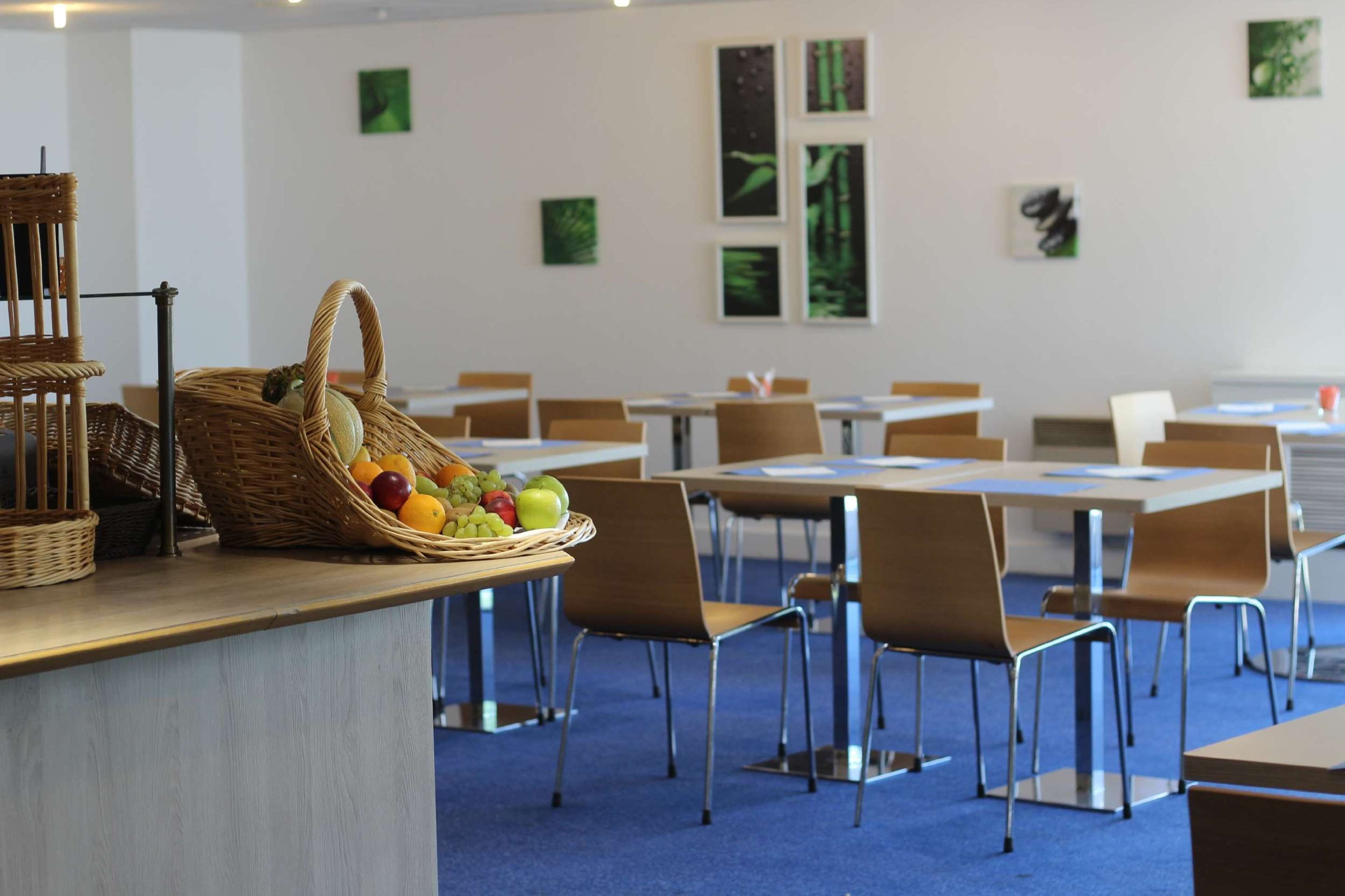 A dining area with tables and chairs, a basket of fruit, and artwork on the walls.