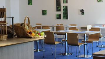 A dining area with tables and chairs, a basket of fruit, and artwork on the walls.