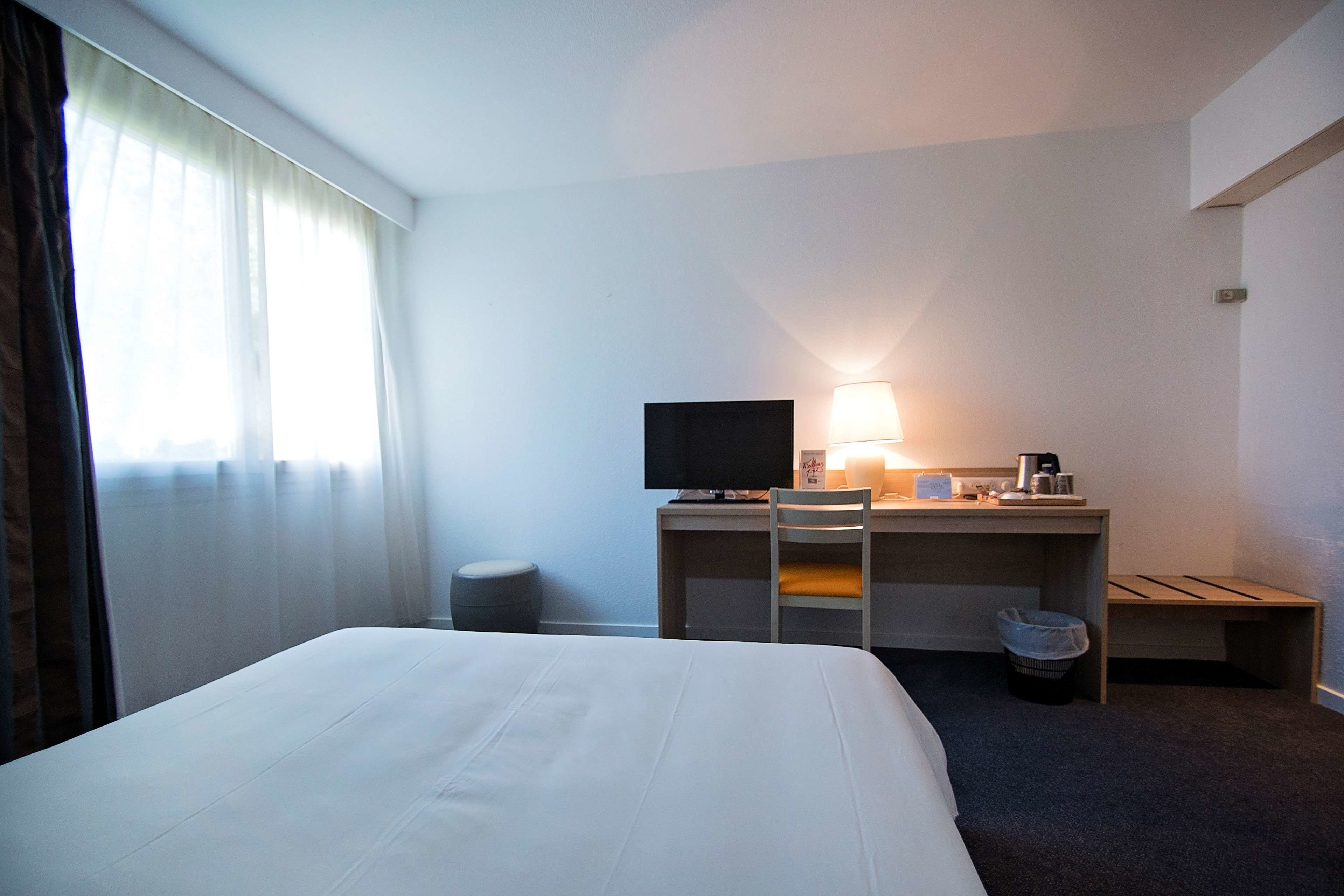 Habitación de hotel con una cama grande, un escritorio con computadora y lámpara, y una televisión.