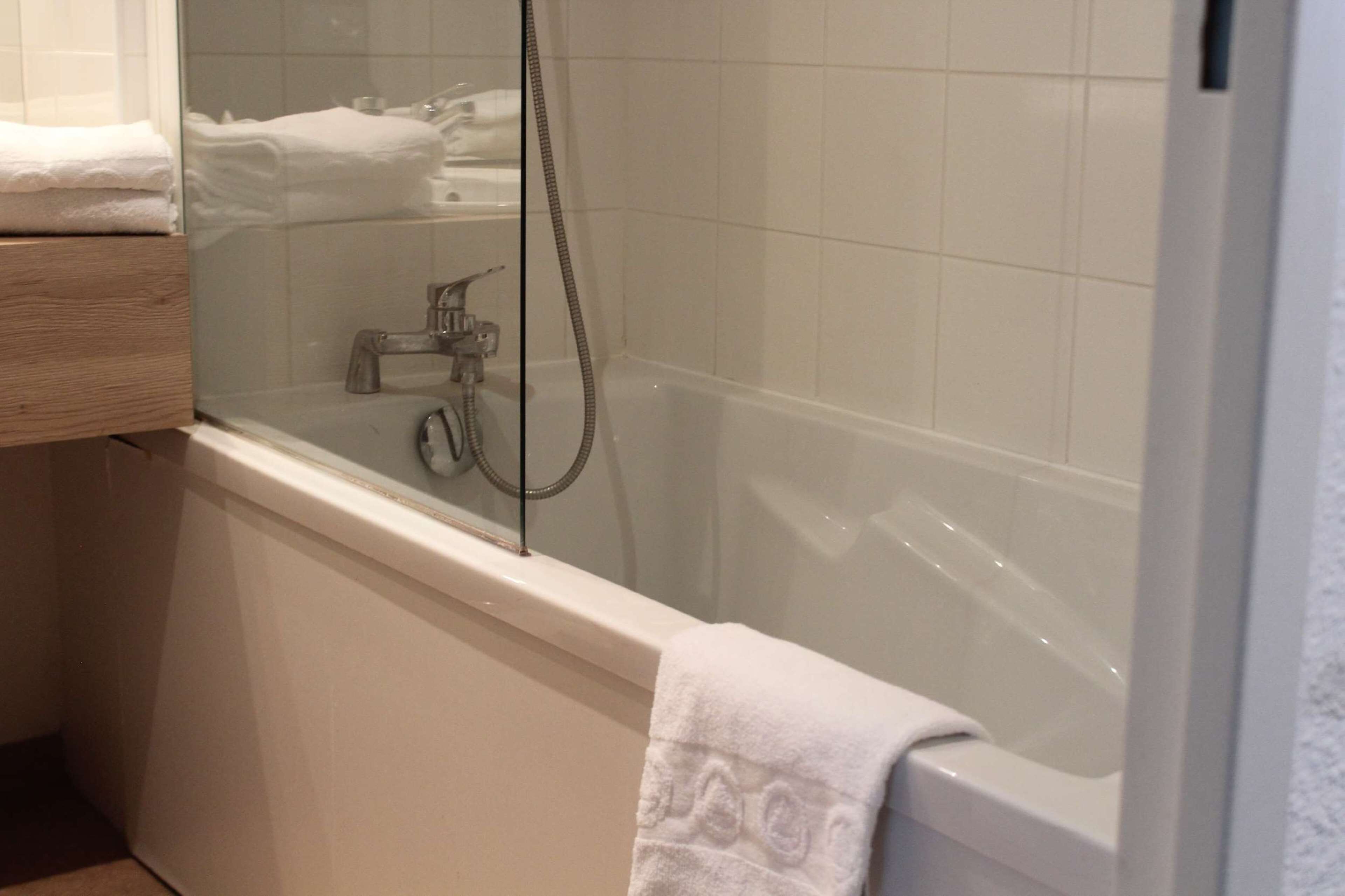 Un baño con ducha envuelta en vidrio, una bañera blanca y un tocador de madera.