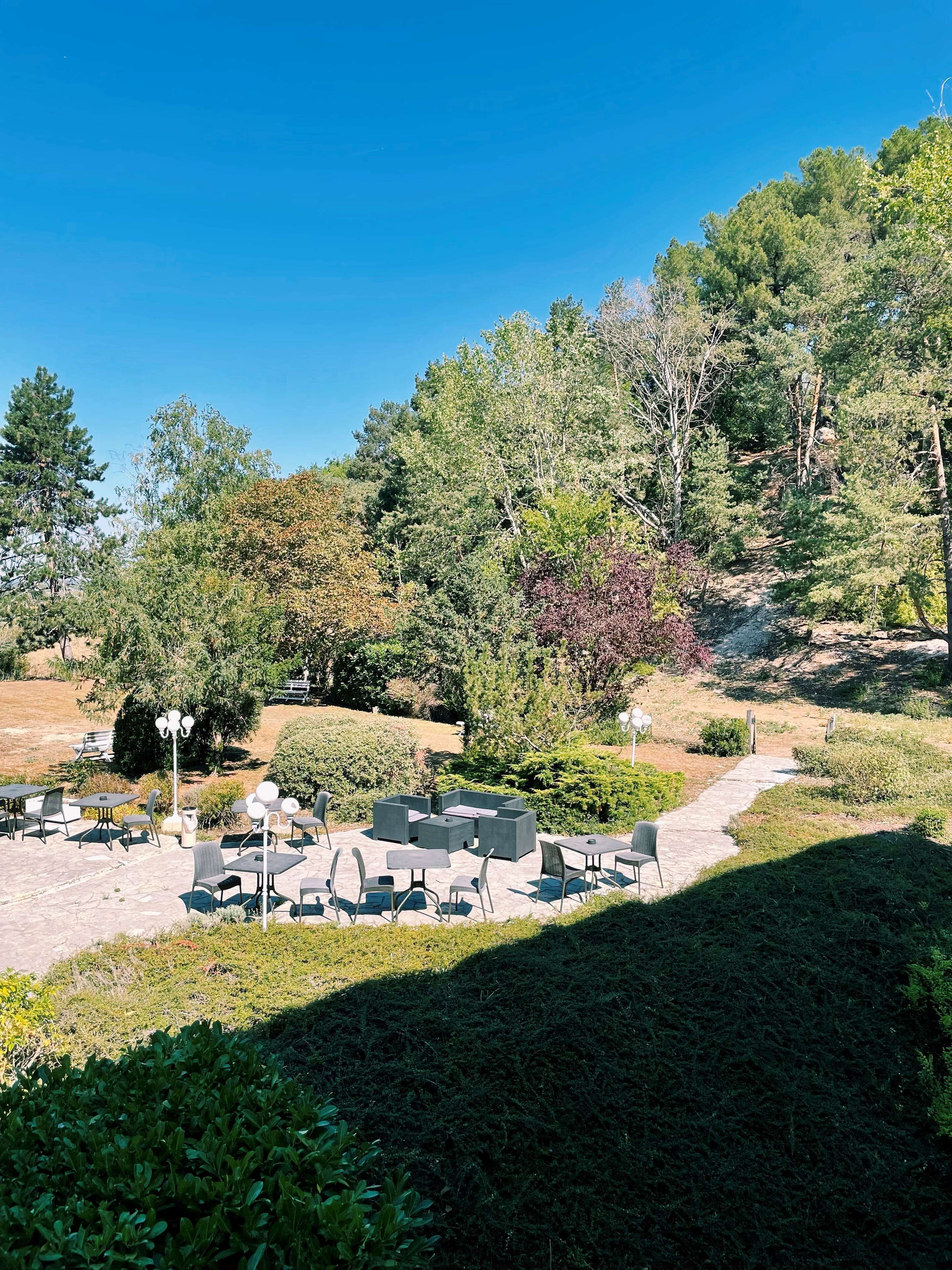 Un espacio al aire libre con mesas y sillas, rodeado de diferentes árboles y arbustos.
