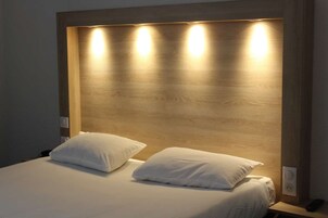 Una cama con dos almohadas y cabecera de madera con iluminación integrada.