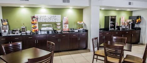 Un restaurante con pared verde, mesas y sillas de madera, y una zona de bufé con diferentes opciones de comida.