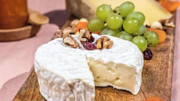 Une portion de fromage, dont on a déjà coupé une tranche, est présentée sur une planche en bois, entourée de raisins, de noix et de fruits secs.