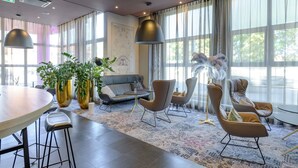 A modern hotel lobby with a round dining table, bar stools, a sofa, and chairs.