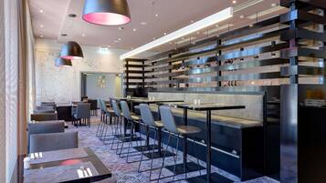 A modern hotel lobby with a bar area, seating, and a decorative wall.