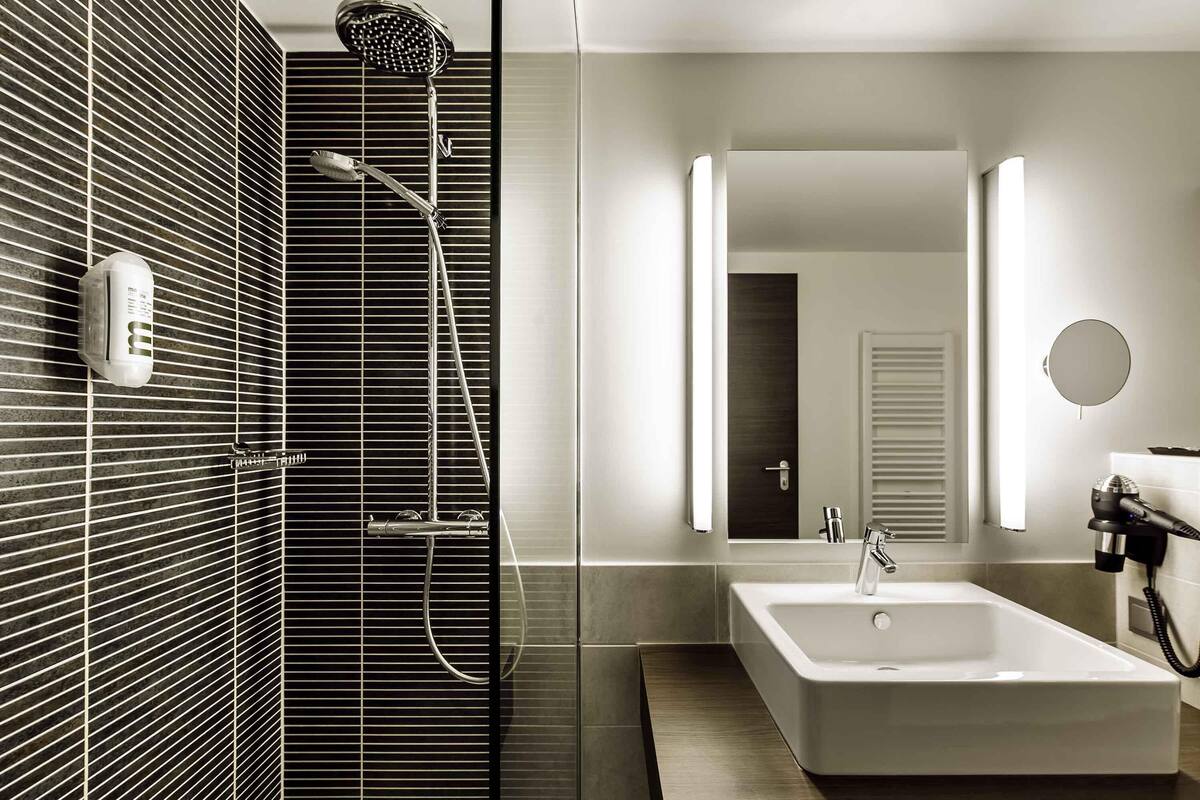 A modern bathroom with a shower, a sink, a mirror, and a towel rack.