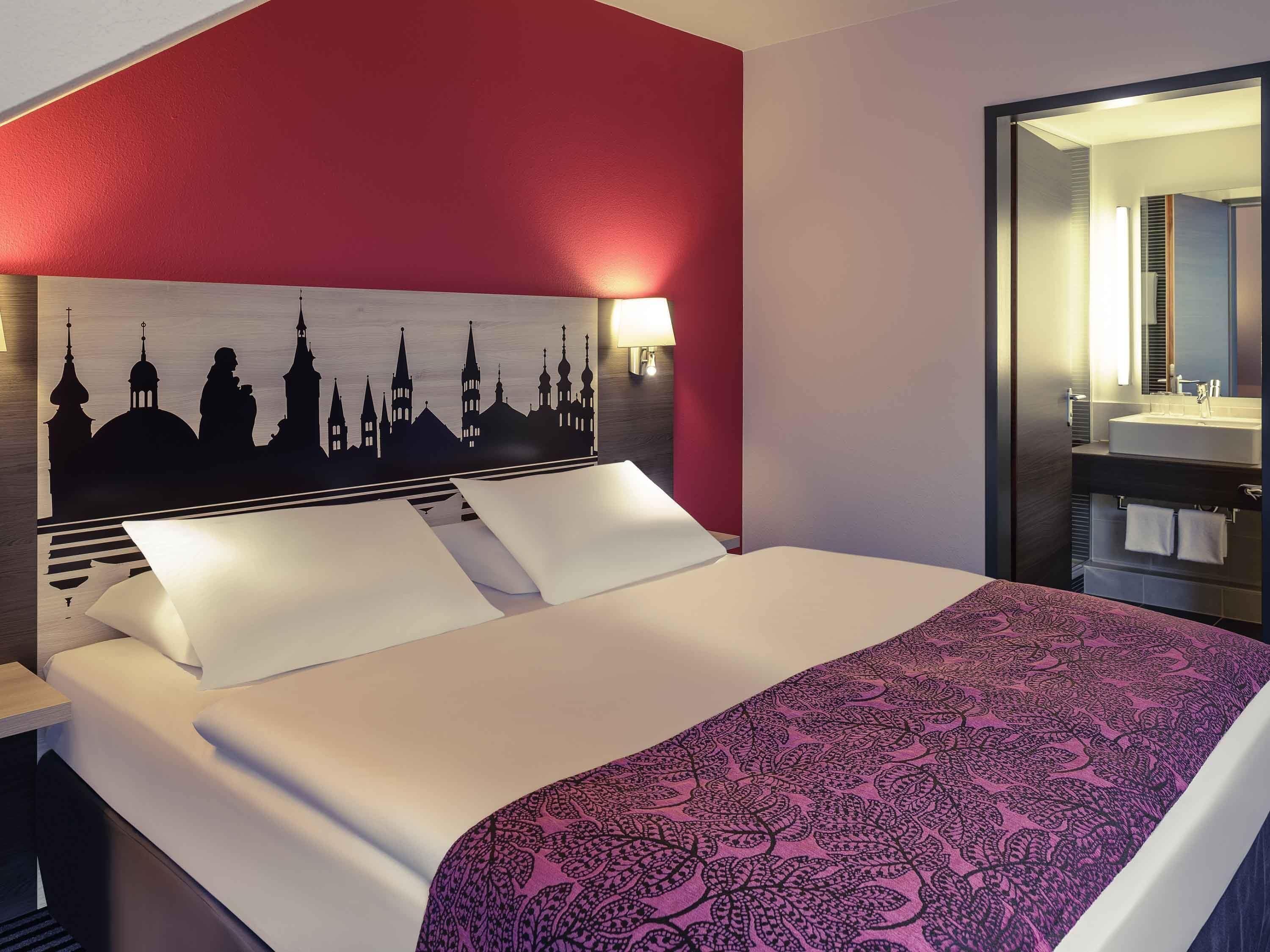 Une chambre d’hôtel avec un lit, une table de chevet, une lampe fixée au mur et un miroir.