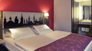 Une chambre d’hôtel avec un lit, une table de chevet, une lampe fixée au mur et un miroir.