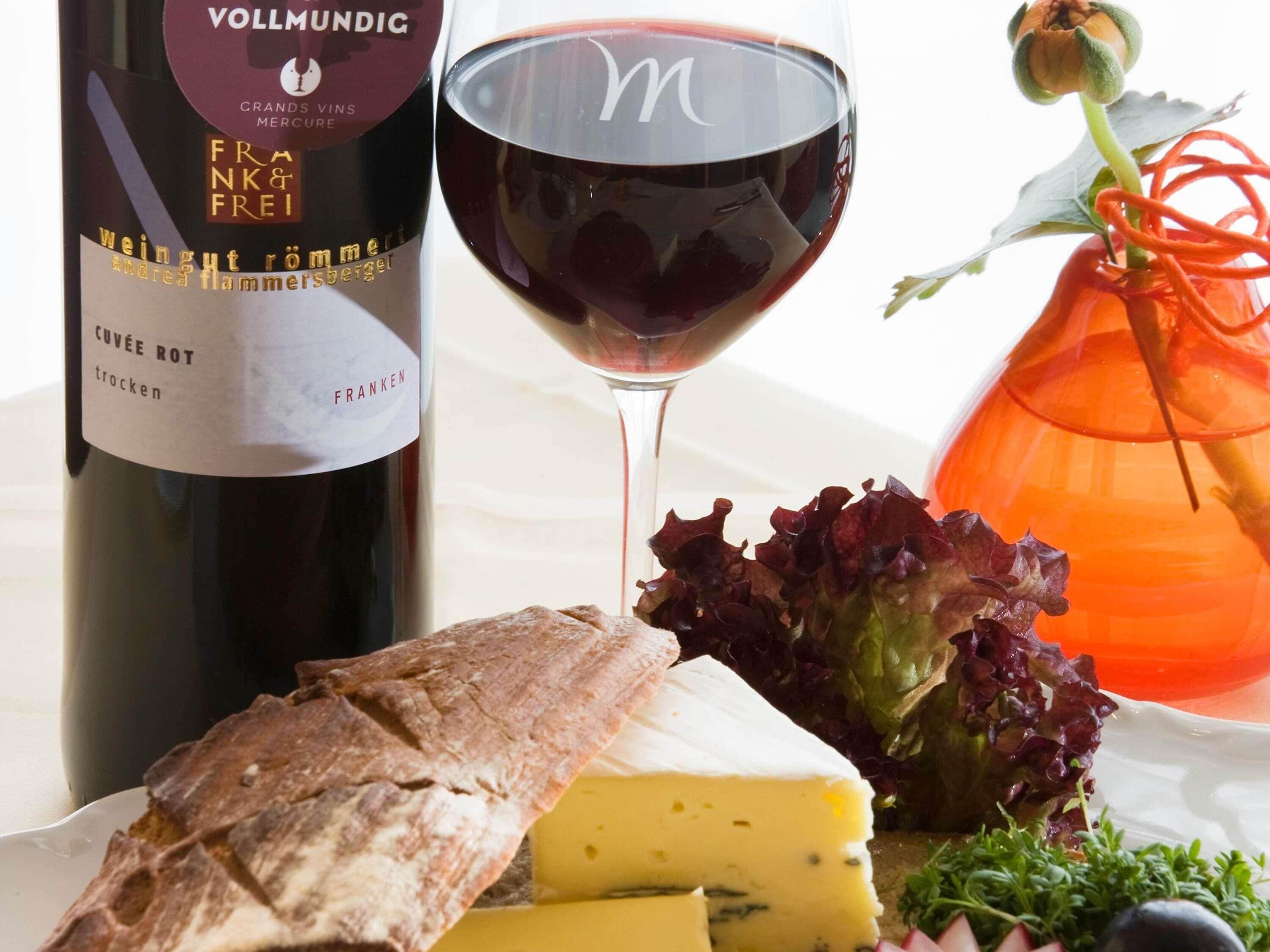 A bottle of wine, a glass of red wine, a loaf of bread, cheese, and a salad.