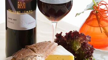 A bottle of wine, a glass of red wine, a loaf of bread, cheese, and a salad.