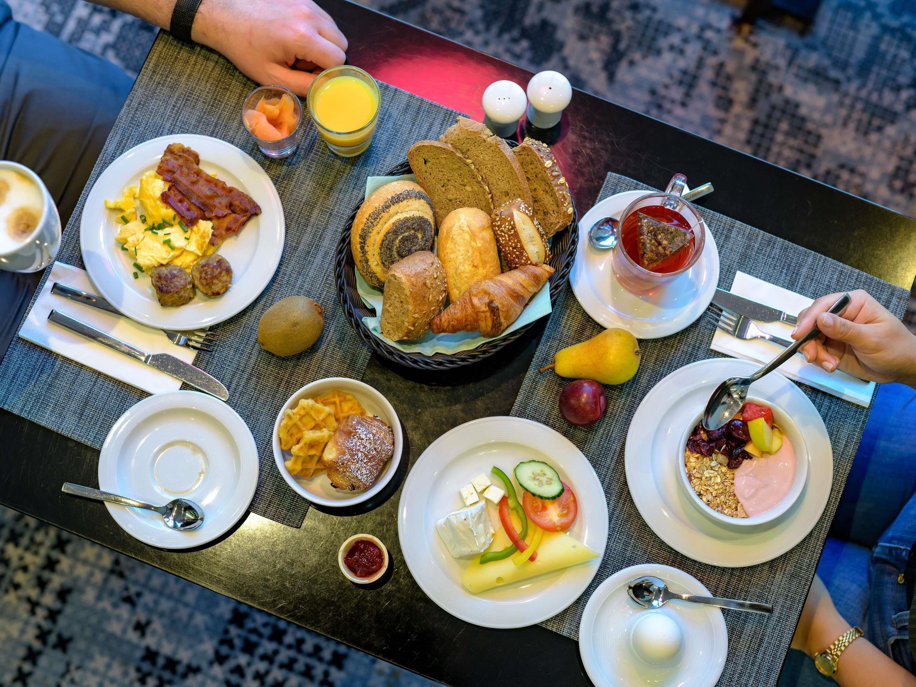 Un bufé de desayuno con diversos platos, como huevos, tocino, pan y frutas.