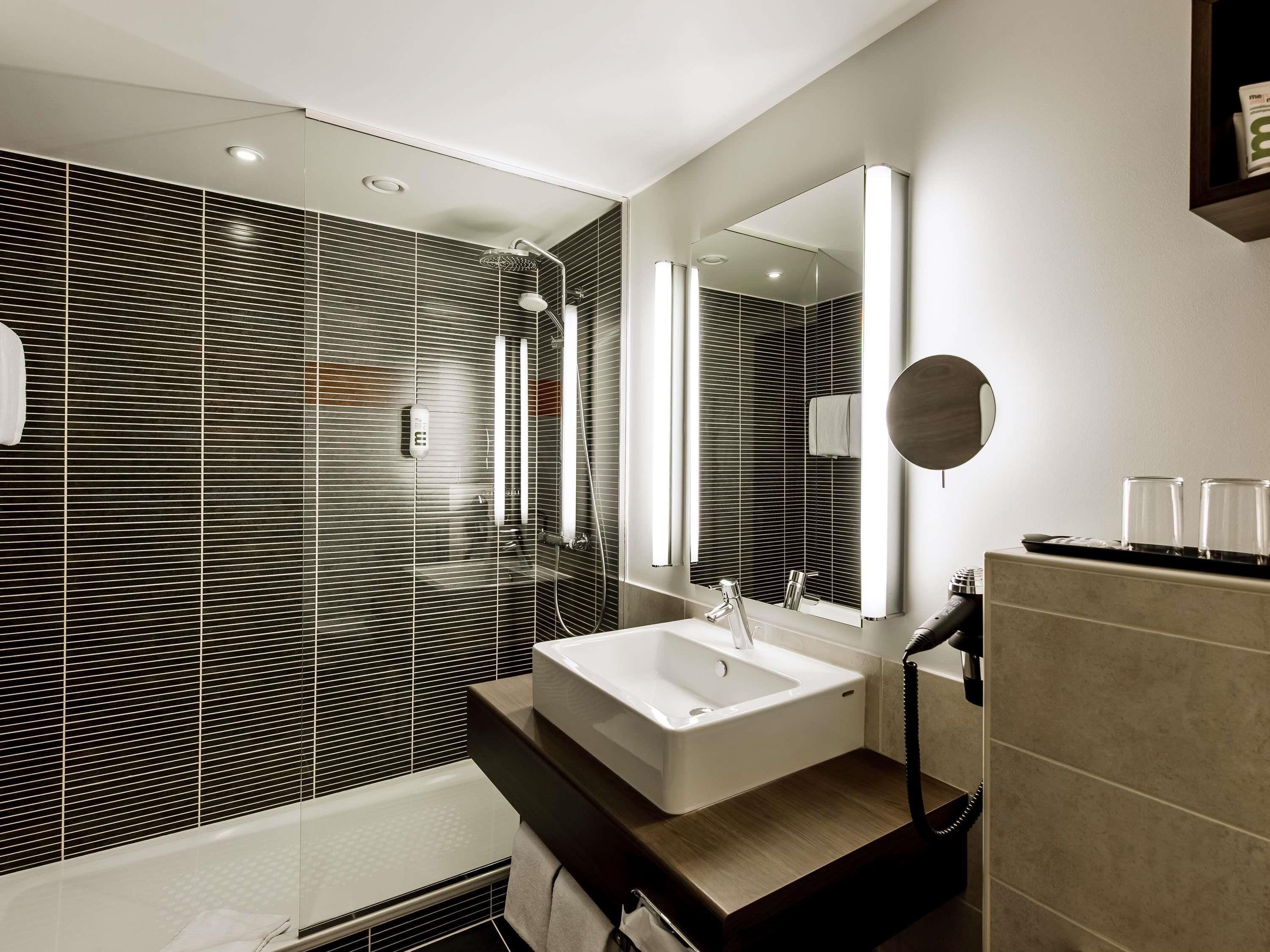 Une salle de bain moderne avec un grand miroir, un lavabo blanc et une douche.