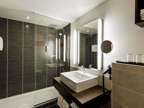 A modern bathroom with a large mirror, a white sink, and a shower. - Mercure Hotel Wuerzburg Am Mainufer (Würzburg)