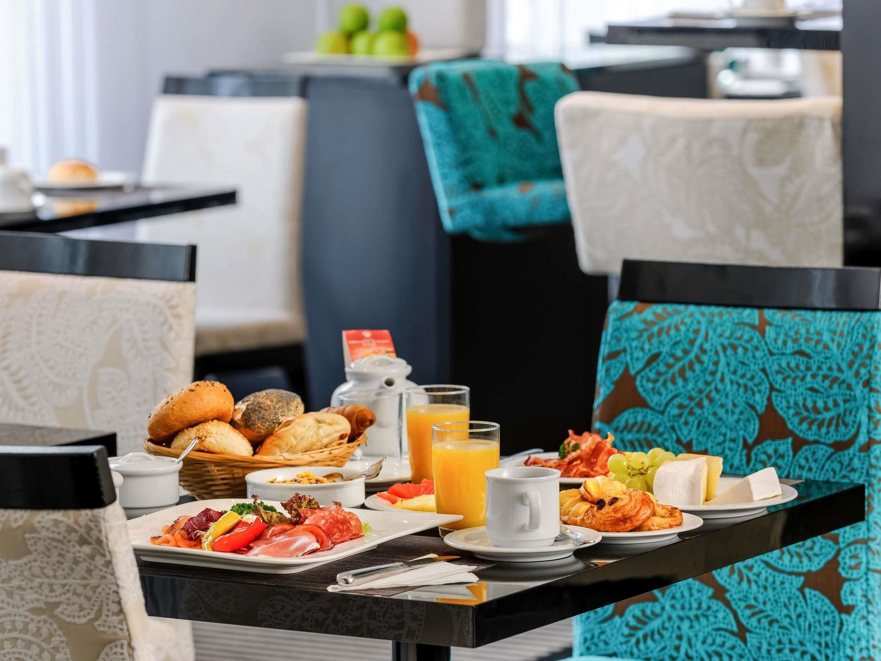 A breakfast buffet with various food items, a glass of orange juice, and a coffee cup on a table.