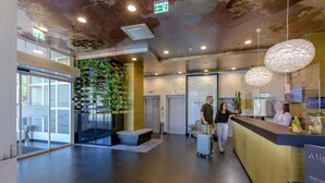 A modern lobby with a reception desk, a staircase, and a glass door with 'WELCOME' signs.
