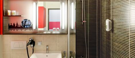 Un baño con lavamanos, espejo, ducha y toallero.
