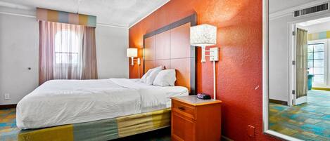 A hotel room with a bed, bedside table, lamp, and a mirror.