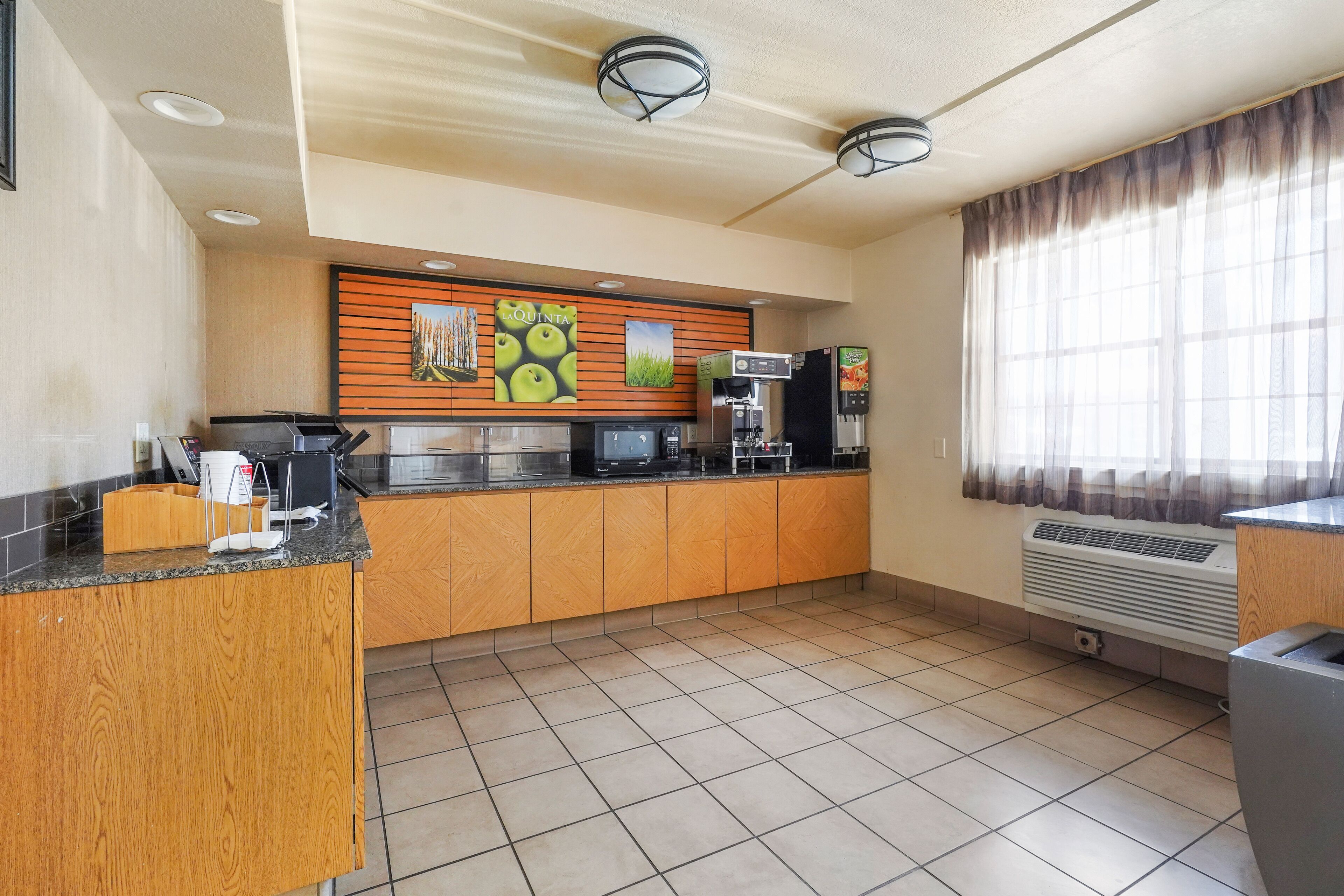 A modern kitchen with wooden cabinets, a countertop with coffee machines, and a large window with curtains.