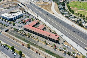An aerial view of a multi-lane highway with a large building with a red roof and a parking lot. - La Quinta Inn by Wyndham Costa Mesa / Newport Beach (Costa Mesa)